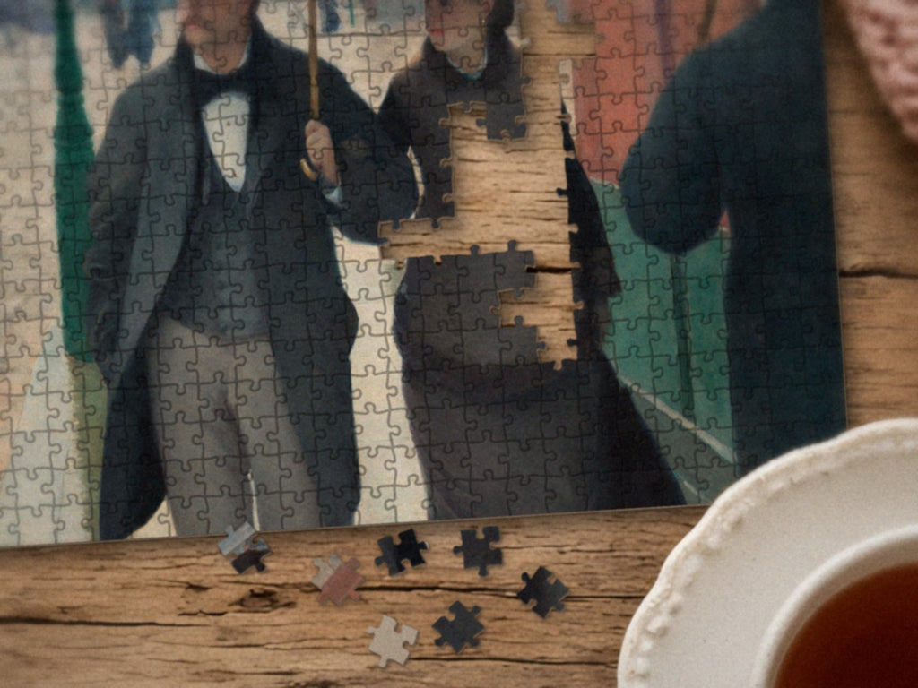 Close-up of the Paris, Just After Rain puzzle on a wood table showing the couple under the gray umbrella, a few pieces still missing, next to a teacup
