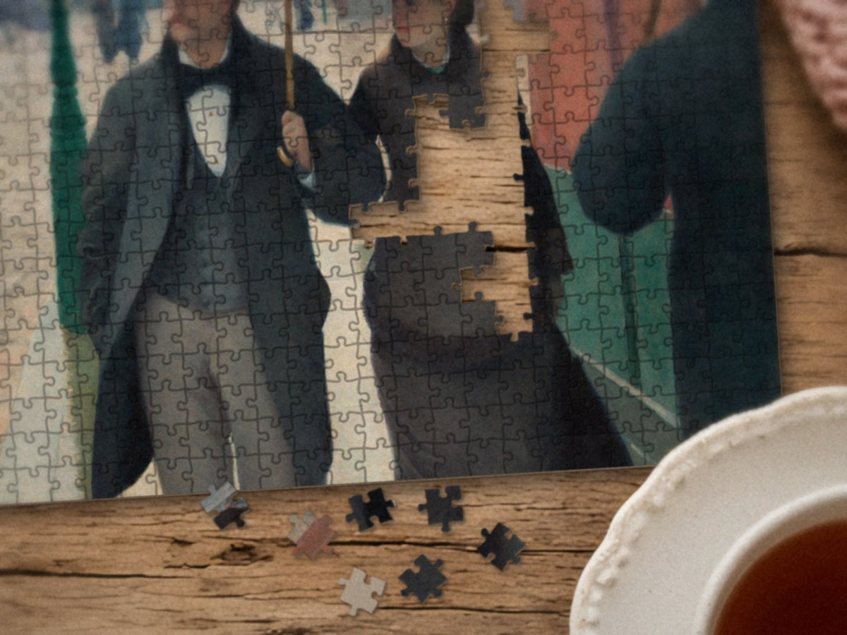 Close-up of the Paris, Just After Rain puzzle on a wood table showing the couple under the gray umbrella, a few pieces still missing, next to a teacup