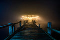 The Carousel at the End of the Pier art puzzle: a glowing carousel with painted horses at the end of a long wooden pier, lit up in thick fog at night
