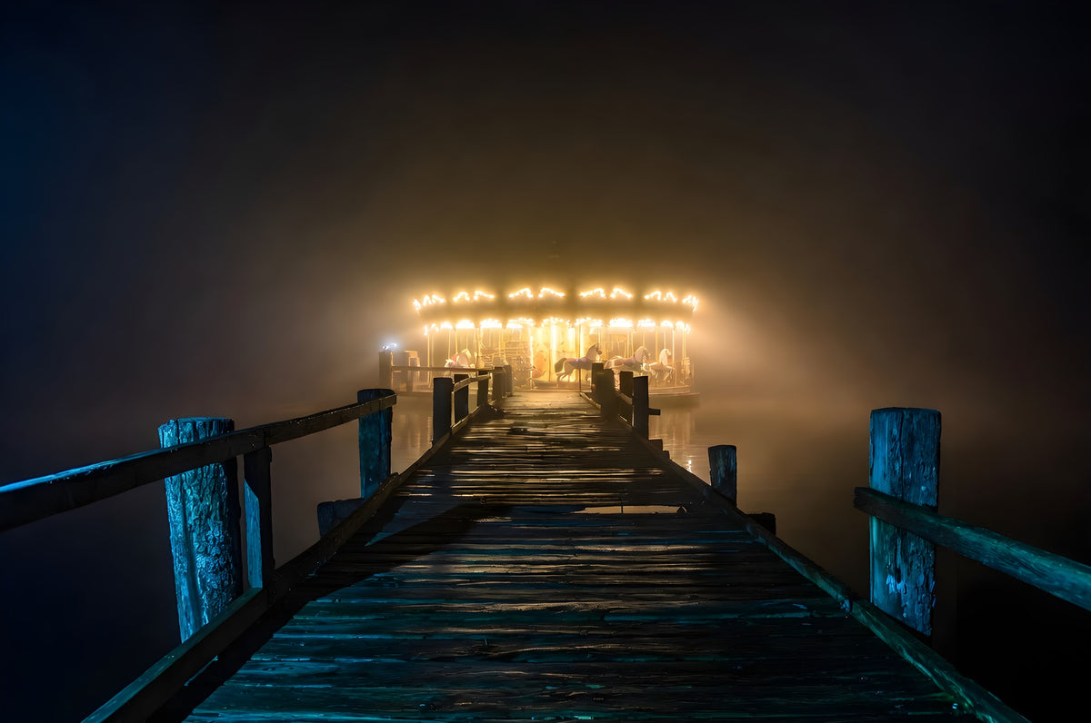 The Carousel at the End of the Pier art puzzle: a glowing carousel with painted horses at the end of a long wooden pier, lit up in thick fog at night