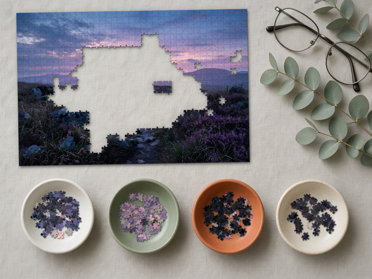 The Heather Road Home 1014 piece puzzle partly assembled on a linen cloth, loose pieces sorted into four small ceramic bowls beside reading glasses and eucalyptus