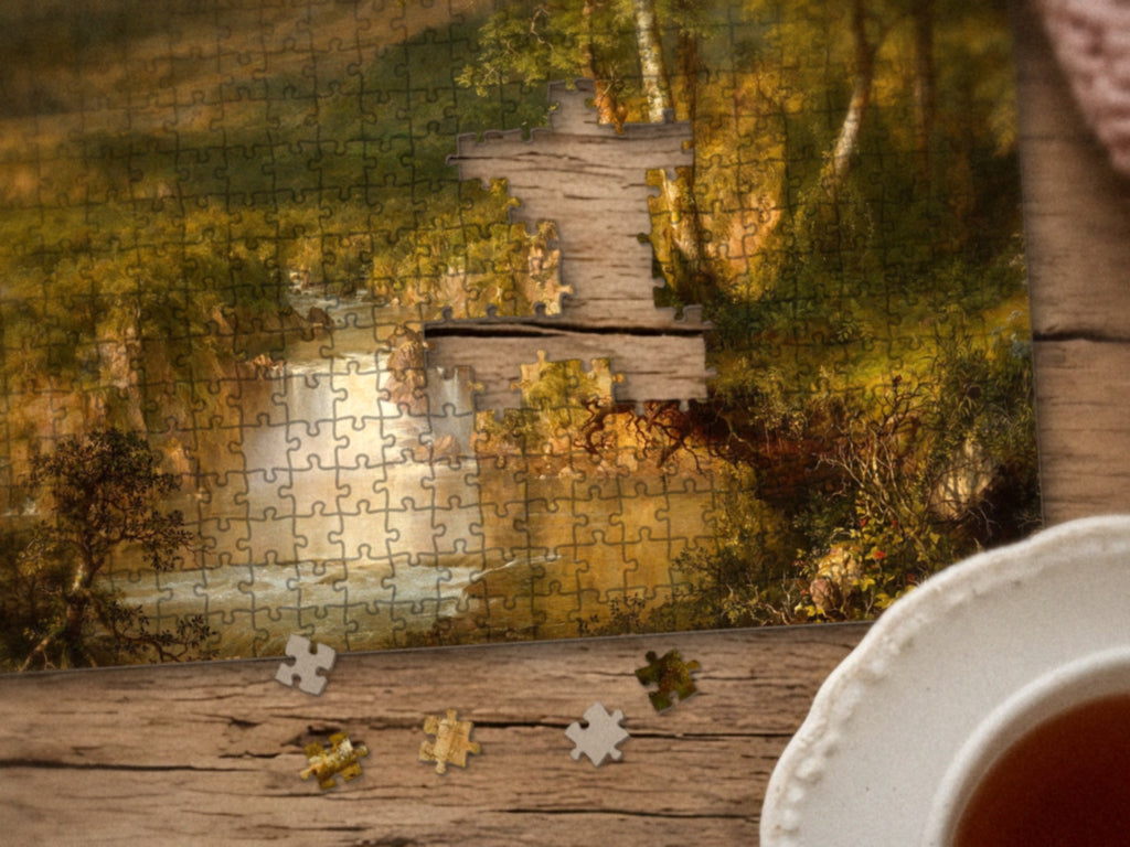 Close-up of the The Hidden Falls of the Andes puzzle on a wood table showing the trees and waterfall, a few pieces still missing, next to a teacup