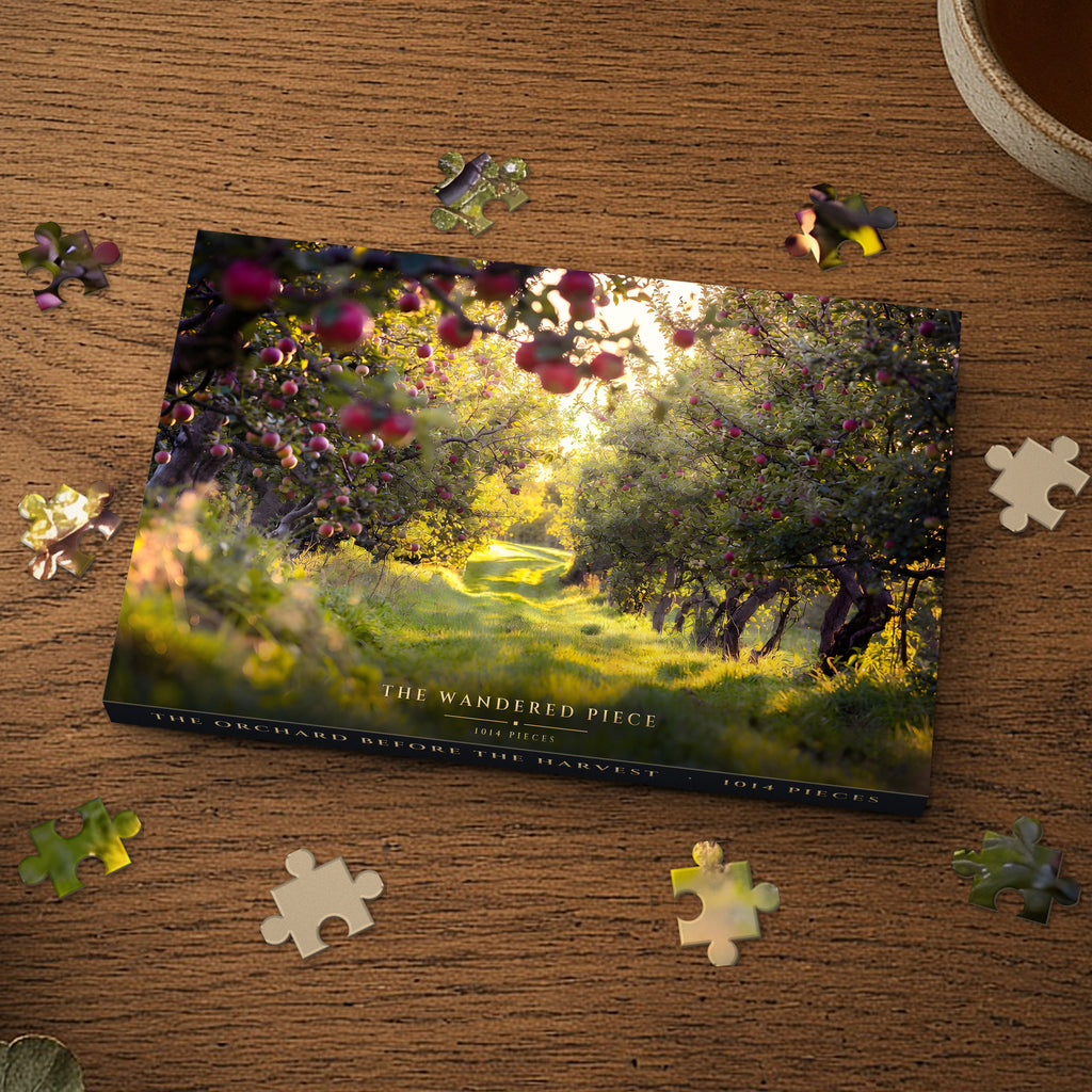 The Orchard Before the Harvest 1014 piece puzzle box on a wood table with loose pieces, box design shown for illustration