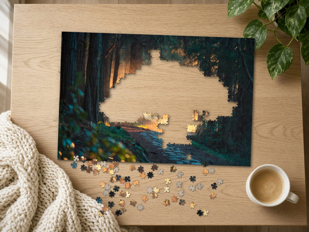 The Path the Giants Lit 1014 piece puzzle half assembled on a light oak table, loose pieces scattered beside a chunky knit throw, a latte and a trailing plant