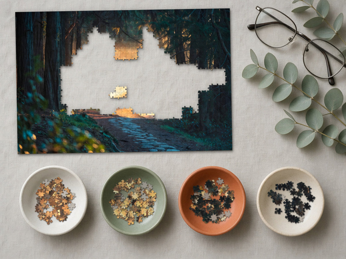 The Path the Giants Lit 1014 piece puzzle partly assembled on a linen cloth, loose pieces sorted into four small ceramic bowls beside reading glasses and eucalyptus