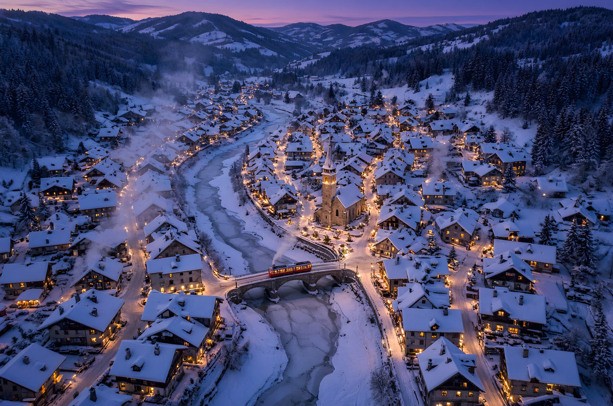 The Village the Snow Tucked In art puzzle: a snowy mountain village at dusk seen from above, hundreds of lit roofs along a frozen river, a church tower in the middle and a small red train crossing a stone bridge
