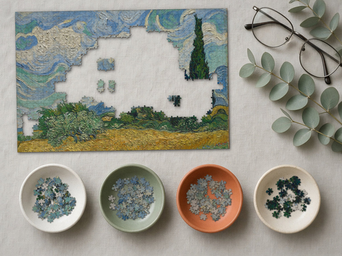 Wind Over the Wheat 1014 piece puzzle partly assembled on a linen cloth, loose pieces sorted into four small ceramic bowls beside reading glasses and eucalyptus